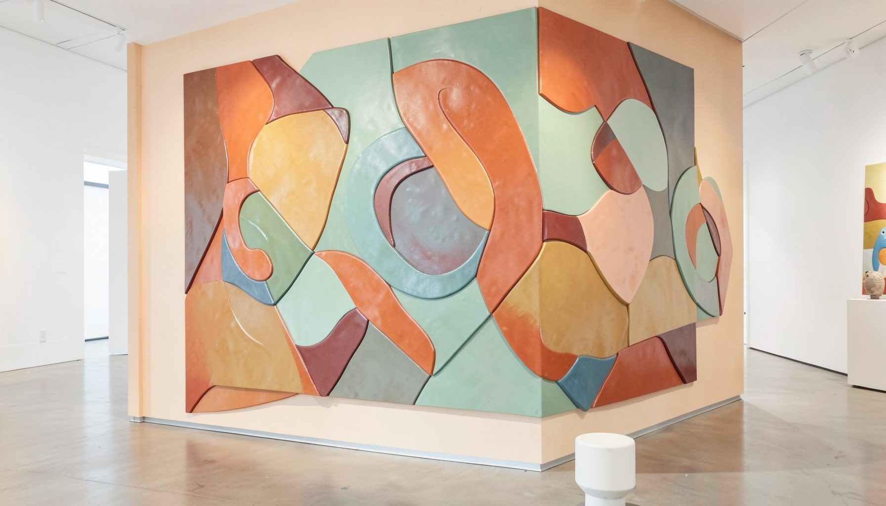 Ceramic wall installation with layered colorful abstract forms in a bright gallery setting, warm terracotta and sage tones