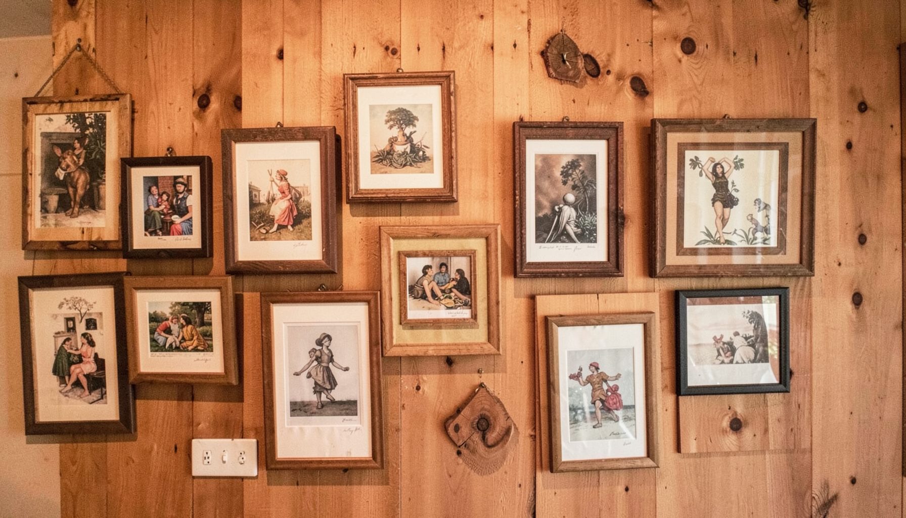 Gallery wall arrangement of small framed artworks and prints in warm wood tones, eclectic and personal