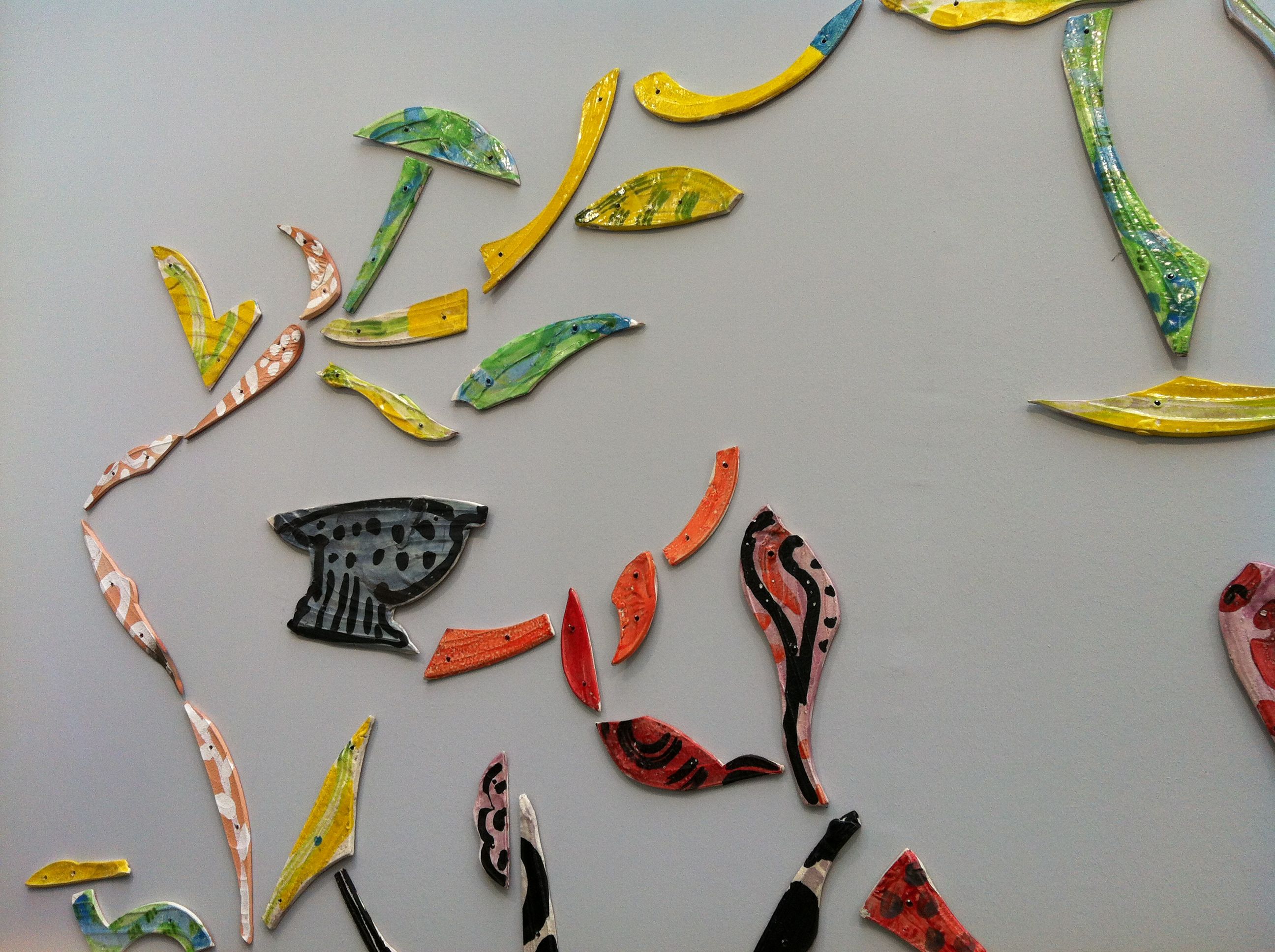 Close-up of painted ceramic fragments in yellow, green, orange, and red hues arranged decoratively on a gray wall