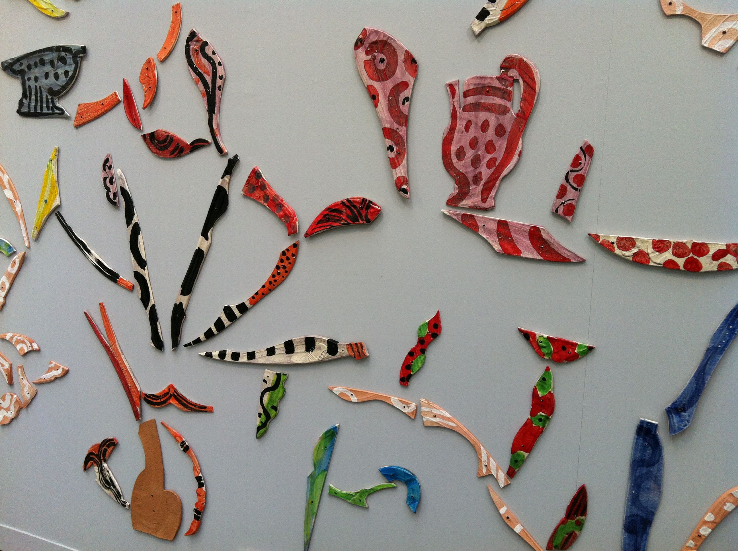 Close-up of colorful painted ceramic fragments shaped like leaves and vessels mounted on a gray wall